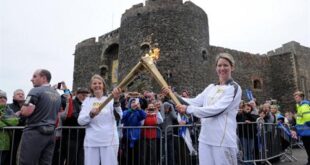 In rhis photo issued by LOCOG shows Kathleen Irvine, left, passes Lisa Hickson the Olympic Flame outside of Carrickfergus Castle in Carrickfergus Northern Ireland during the Olympic Torch Relay Sunday June 3, 2012. (AP Photo/ Ben Birchall/LOCOG)
